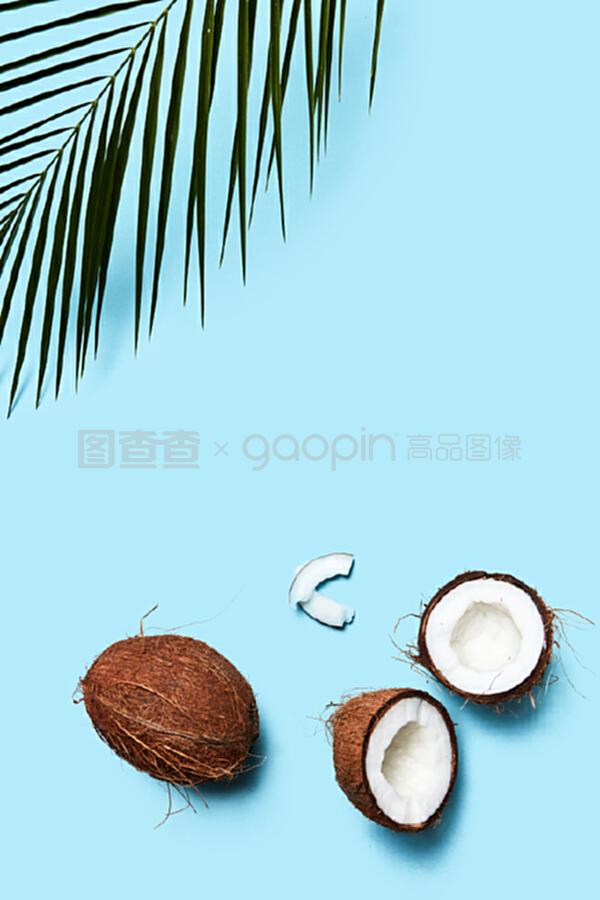 一片椰子和整個椰子,在藍色背景上有一片棕櫚綠葉。食物成分。平鋪。一個由有機的一半和一個椰子組成的美麗組成的藍色背景裝飾著一塊飾板,上面有一片平鋪。